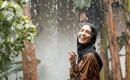 A smiling woman standing among tropical plants during rainfall in Zanzibar