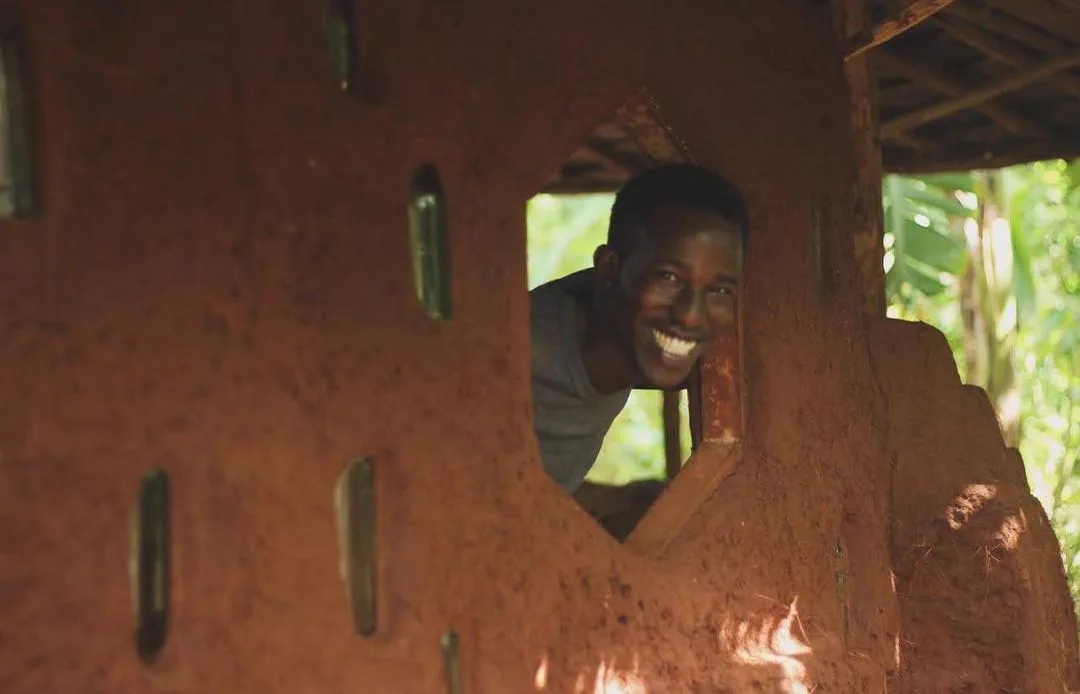 A smiling builder framed by a hand-shaped opening in an earth wall