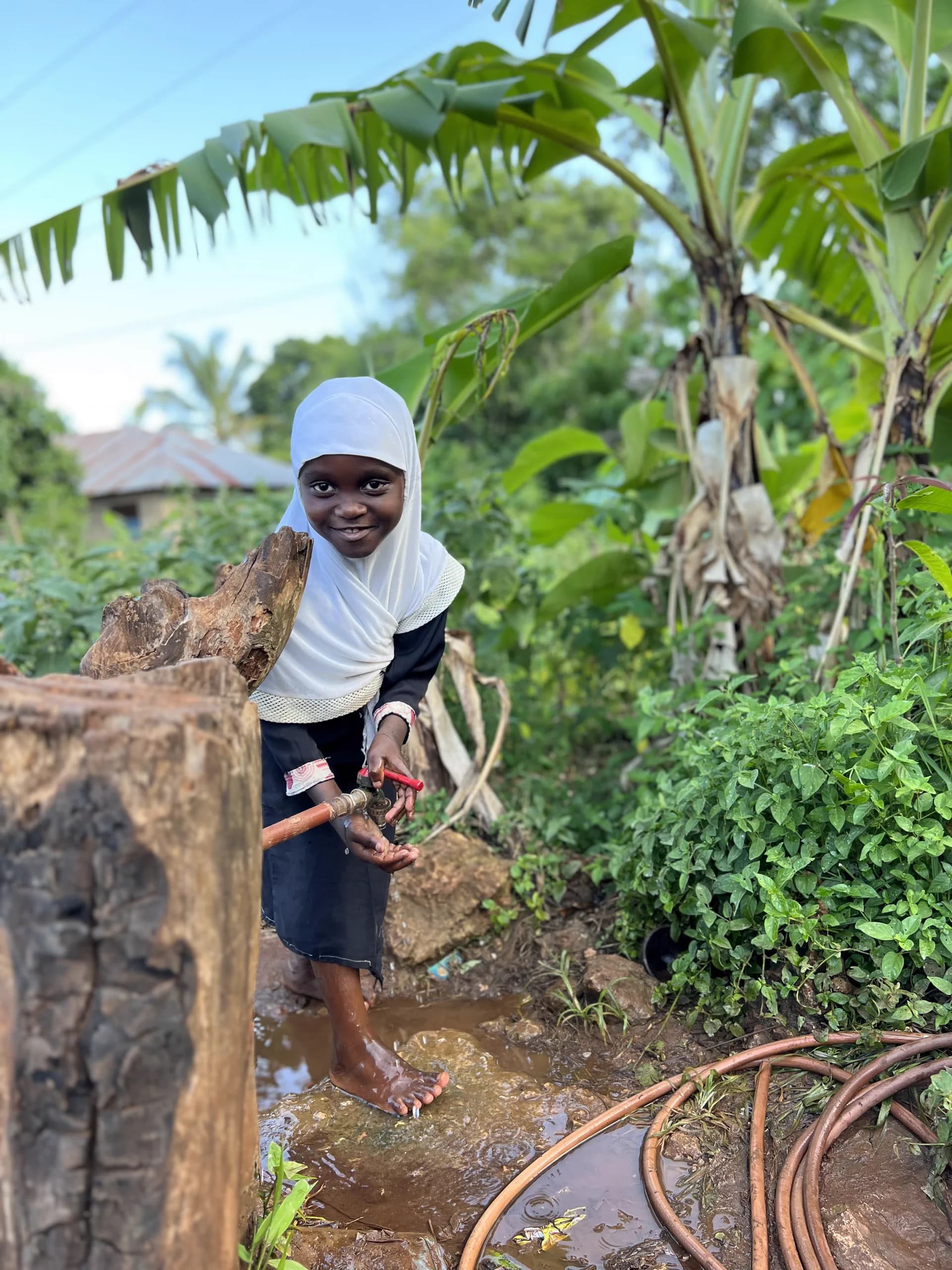 A young learner washing her hands beside a school garden