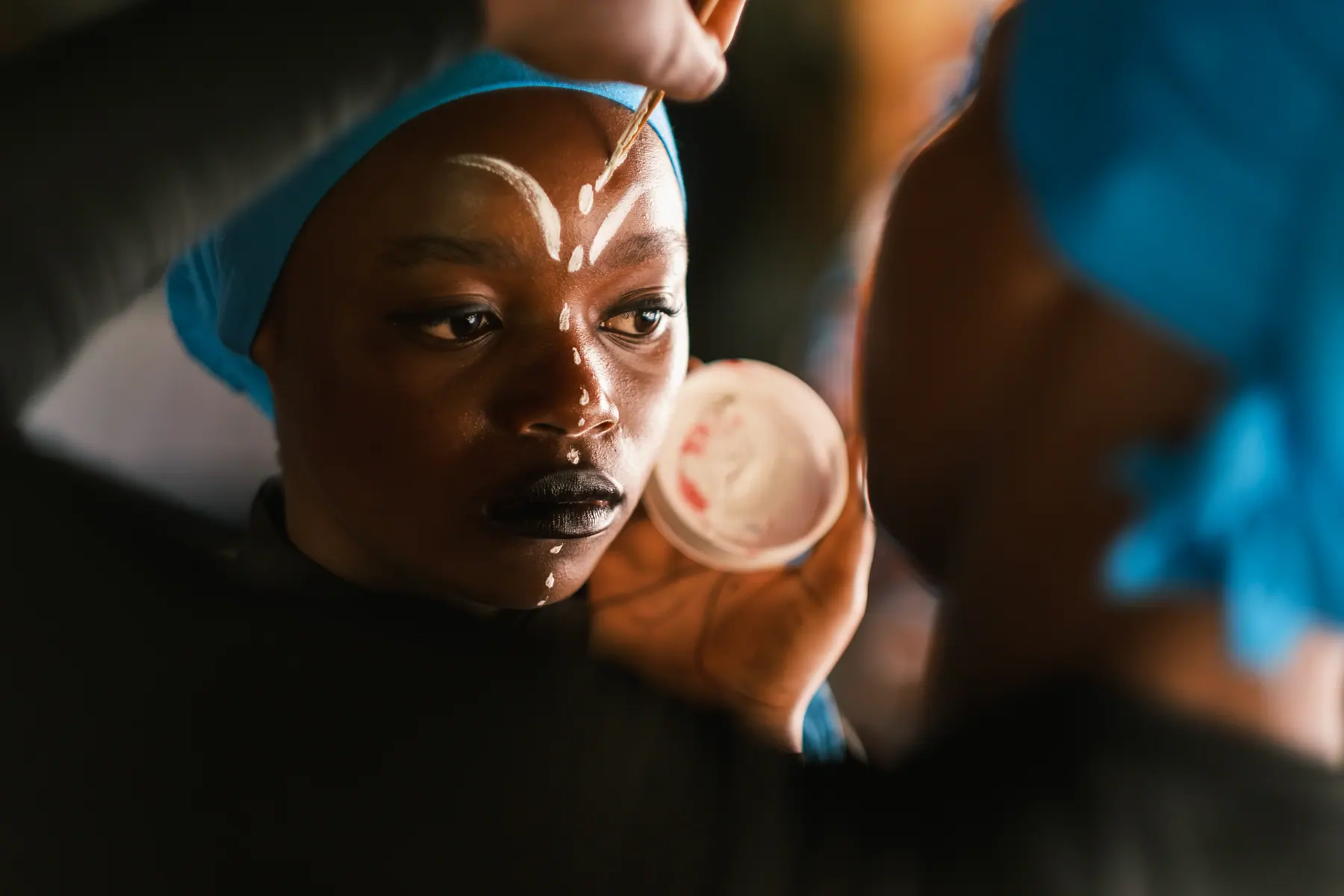 A young Sawa Ensemble performer receiving white stage markings before a performance