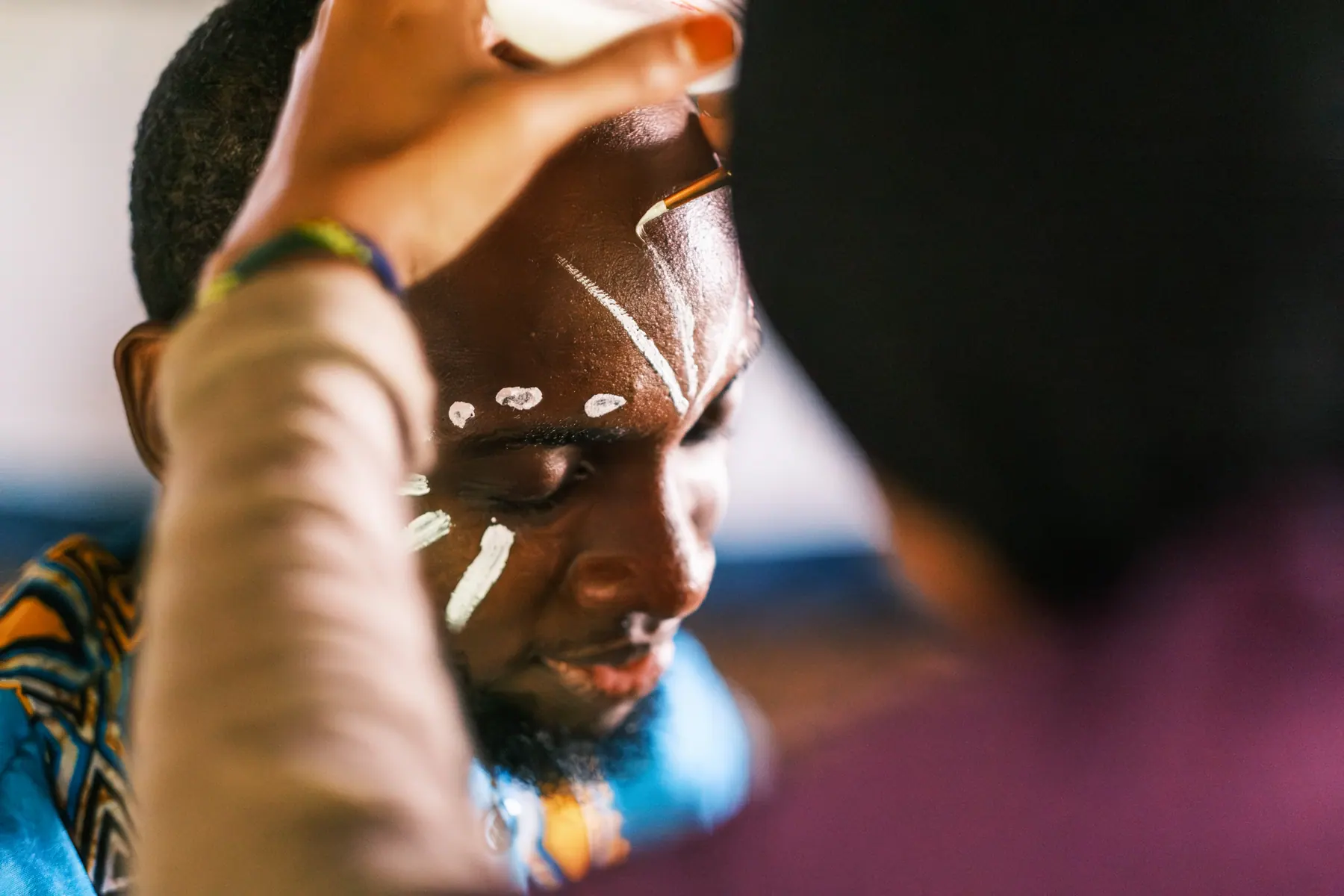 A Sawa Ensemble performer having white stage markings painted on his face