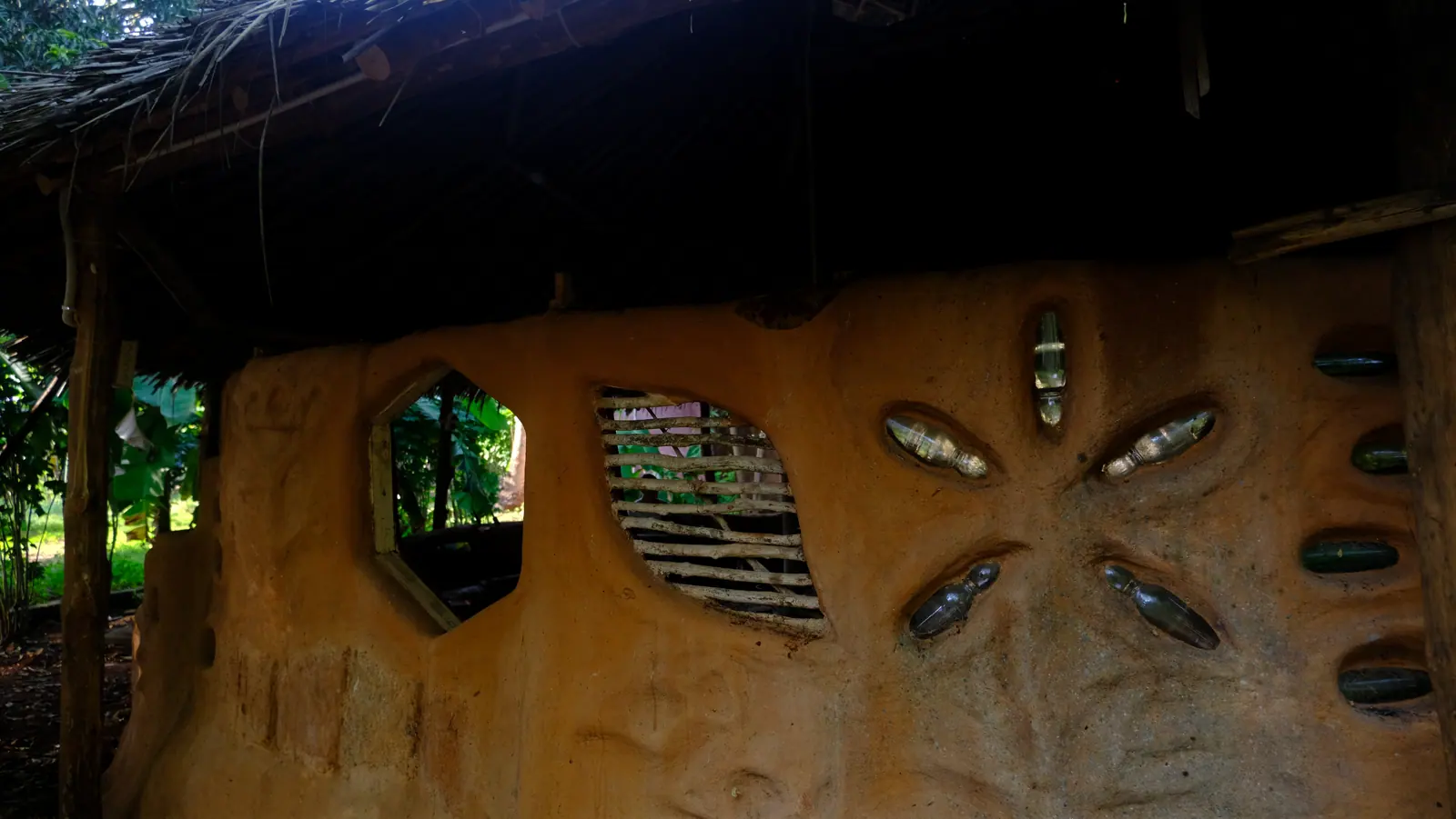 Hand-shaped Earth House wall with reused glass bottles and irregular windows