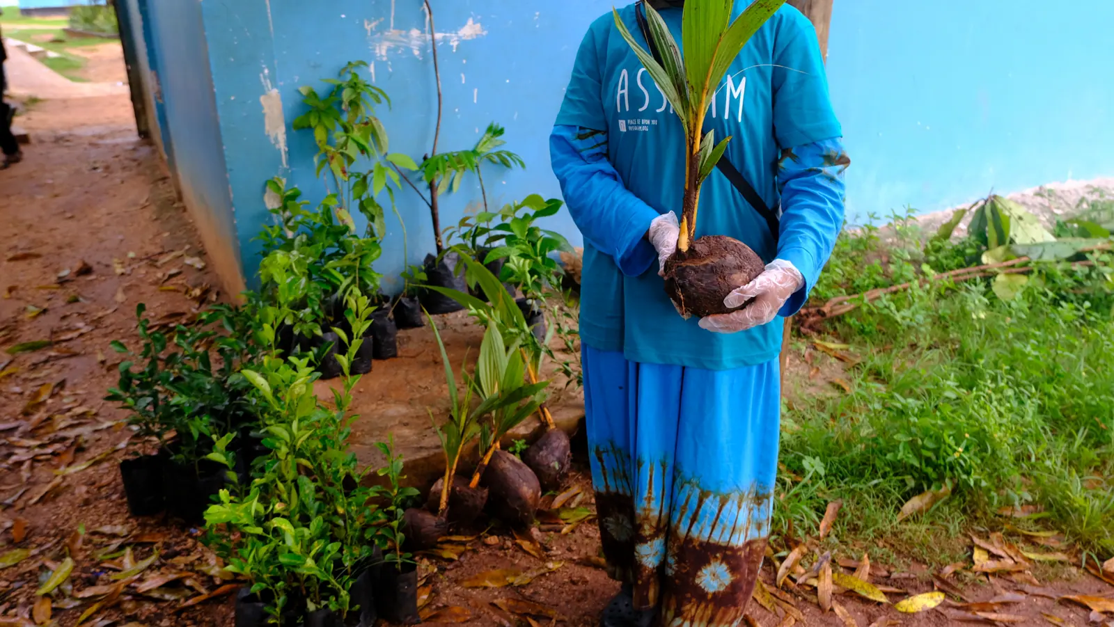 An Assalam participant holding a coconut seedling beside a Food Forest sign